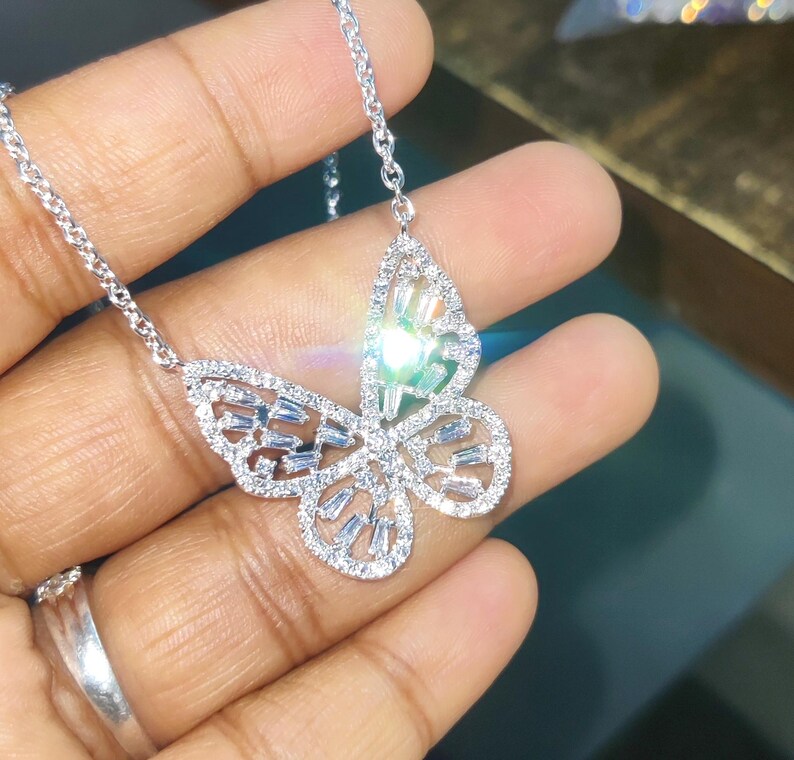 Peut inclure: Un collier pendentif papillon argent&eacute;. Le motif papillon est incrust&eacute; de petits cristaux &eacute;tincelants. La cha&icirc;ne du collier est d&eacute;licate et &eacute;galement argent&eacute;e. Le collier est pr&eacute;sent&eacute; sur un fond neutre.