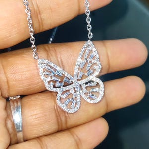 Peut inclure: Un collier pendentif papillon argent&eacute;. Le motif papillon est incrust&eacute; de petites pierres scintillantes. La cha&icirc;ne du collier est &eacute;galement argent&eacute;e et d&eacute;licate. Le bijou est pr&eacute;sent&eacute; sur un fond sombre.