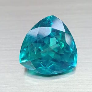 May include: A faceted, triangular gemstone with a vibrant teal color. The gem's surface reflects light, showcasing its intricate cuts and angles. The gemstone is a striking example of fine jewelry.