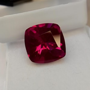 Può includere: Una gemma di rubino sfaccettata a taglio cuscino. La pietra ha un colore rosso intenso e saturo con brillanti riflessi interni. La gemma è posta su uno sfondo bianco. Per gioielli.