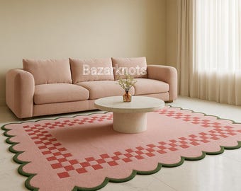 May include: A pink area rug with a scalloped edge and a red and pink checkered border. The rug is in a living room setting with a pink sofa, a round coffee table, and the text "Bazarknots".