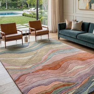 May include: A large, rectangular rug with a flowing, wave-like design in shades of peach, pink, orange, green, and blue. The rug is placed on a wooden floor in a living room setting, with furniture visible.