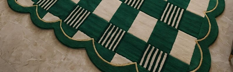 May include: A decorative rug with a scalloped edge. The rug features a green and white checkered pattern with alternating stripes. A gold-colored trim outlines the edge of the rug.