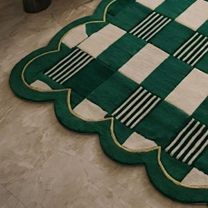 May include: A green and cream-colored rug with a scalloped edge. The rug features a checkered pattern with alternating green and cream squares, some with black and white stripes. A gold trim outlines the edge.