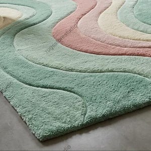 May include: A pastel-colored area rug with a wavy design. The rug features soft, plush textures in shades of mint green, pink, cream, and light blue. The rug's design creates a flowing, organic pattern, adding a touch of elegance to any room.