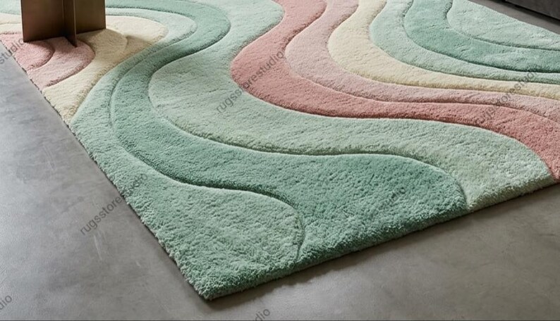 May include: A pastel-colored area rug with a wavy design. The rug features soft, plush textures in shades of mint green, pink, cream, and light blue. The rug's design creates a flowing, organic pattern, adding a touch of elegance to any room.