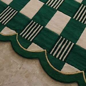 May include: A green and white checkered rug with a scalloped edge. The rug features alternating squares of solid green and white, with some green squares containing black and white stripes. The edge is green with a gold trim.