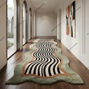 May include: An elongated, irregular-shaped area rug featuring a central pattern of black and white wavy lines. The rug is bordered by a thick band of burnt orange, followed by a wider, sage green outer edge with a soft, textured pile finish.