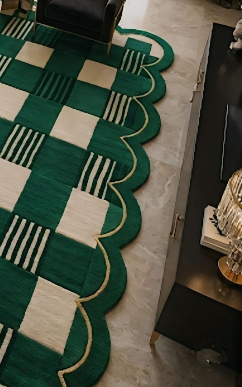 May include: A green and cream-colored area rug with a unique scalloped edge. The rug features a checkerboard pattern with alternating green squares and cream squares, some with white stripes. A gold trim outlines the edge.