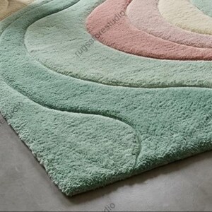 May include: A soft, plush area rug with a wavy design in pastel colors. The rug features shades of light green, pink, and cream, creating a calming and inviting aesthetic. The textured surface adds depth and visual interest to the floor covering.