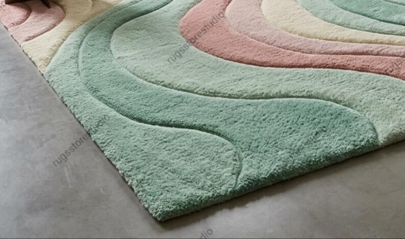 May include: A soft, plush area rug with a wavy design in pastel colors. The rug features shades of light green, pink, and cream, creating a calming and inviting aesthetic. The textured surface adds depth and visual interest to the floor covering.