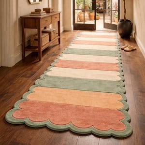 Puede incluir: Una alfombra de pasillo a rayas con borde festoneado. La alfombra presenta rayas horizontales en tonos melocotón, crema y verde salvia. Está colocada sobre un suelo de madera oscura en un pasillo.