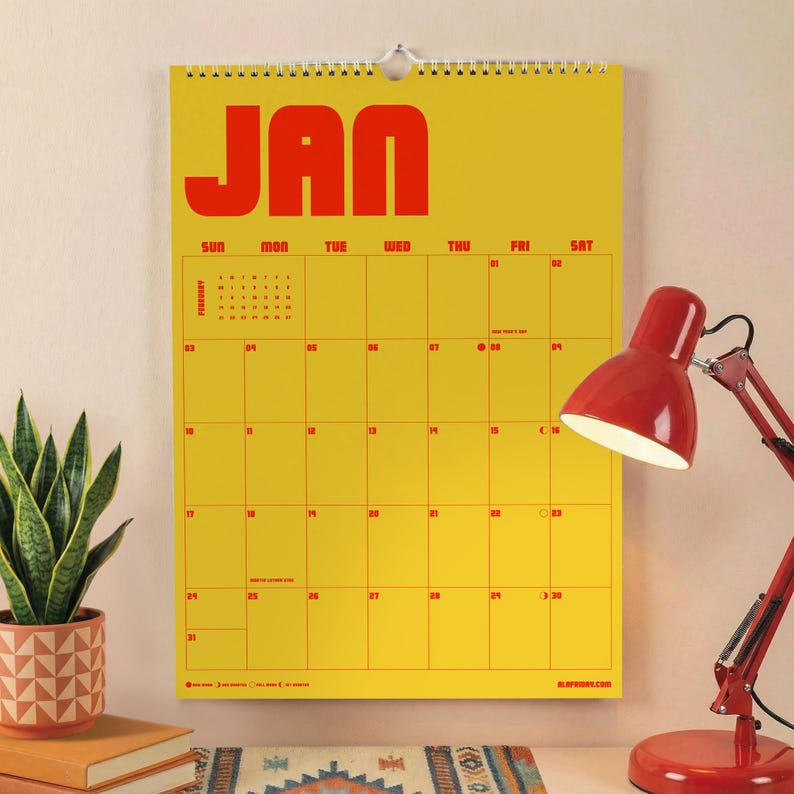 Puede incluir: Un calendario de pared con fondo amarillo brillante y texto rojo en negrita que dice JAN en la parte superior. La cuadr&iacute;cula muestra los d&iacute;as del mes con n&uacute;meros y encabezados rojos. Tiene una espiral blanca y un peque&ntilde;o calendario de febrero.