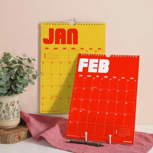 Puede incluir: Un calendario de pared amarillo para enero y un calendario de pared rojo para febrero, ambos con letras de bloque en negrita para los nombres de los meses y una cuadr&iacute;cula para los d&iacute;as. Los calendarios est&aacute;n encuadernados en espiral.