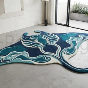May include: A large, irregularly shaped area rug designed in the likeness of a manta ray. The rug features a vibrant colour palette of deep navy blue, teal, and white, with intricate, flowing patterns that mimic the movement of ocean waves.