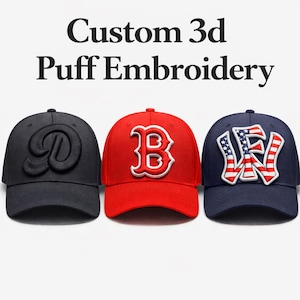 May include: Three baseball caps with custom 3D puff embroidery. The caps are black, red, and navy blue. The black cap has a stylized "D", the red cap has a "B", and the navy cap has "NY" with an American flag design.