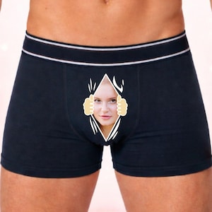 May include: Navy blue boxer shorts with a white waistband and a torn design revealing a woman's face. The background features roses and gift boxes, suggesting a romantic theme.