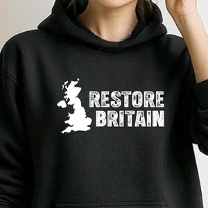 Könnte beinhalten: Schwarzer Kapuzenpullover mit weißer Grafik der Britischen Inseln und dem Text "RESTORE BRITAIN". Der Pullover hat eine Vordertasche und eine Kapuze mit Kordelzug. Das Design ist mittig platziert.