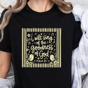May include: A black short-sleeved t-shirt featuring a yellow graphic print. The design includes vertical stripes, floral accents, musical notes, two birds, and the text: I will sing of the goodness of God PSALM 89:1.