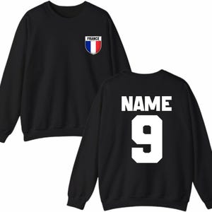 May include: Black sweatshirt with the word "NAME" and the number "9" in white on the back. A small shield with the French flag and the word "FRANCE" is on the front.