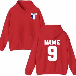 May include: A red hoodie with a front pocket and a hood. The front features a small shield with the word "FRANCE" and the French flag colors. The back displays the word "NAME" above the number "9" in white.