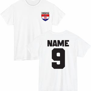 May include: White t-shirt with the Croatian flag emblem on the front and the word "NAME" above the number "9" on the back. The Croatian flag emblem is a shield with a red and white checkered pattern and the word "CROATIA" above it.
