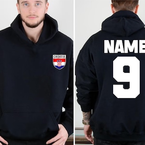 May include: Black hooded sweatshirt with the Croatian coat of arms on the front. The back of the sweatshirt displays the word "NAME" above the number "9" in white block letters. The sweatshirt has a front pocket.