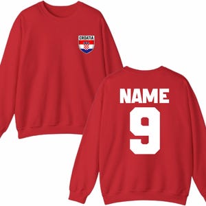 May include: Red sweatshirt with the Croatian flag emblem on the front and the word "NAME" and the number "9" on the back. The sweatshirt is a crew neck style.