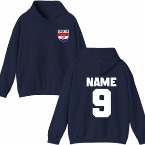 May include: Navy blue hoodie with a front pocket and hood. The front features a Croatia crest. The back displays the word "NAME" above the number "9" in white block letters. A casual, sporty garment.