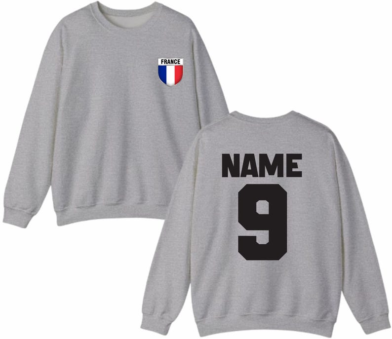 May include: A heather gray sweatshirt with a crew neck. The front features a small patch with the word "FRANCE" and a blue, white, and red shield design. The back displays the word "NAME" above the number "9" in black.