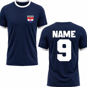 Puede incluir: Camiseta de f&uacute;tbol azul marino con ribetes blancos en el cuello y las mangas. La parte delantera presenta un escudo de Croacia y la palabra "CROATIA". La parte trasera muestra la palabra "NAME" sobre el n&uacute;mero "9".