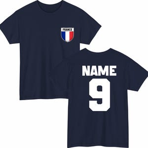 May include: Navy blue t-shirt with a French flag emblem on the chest. The back of the shirt displays the word "NAME" above the number "9" in white block letters. A classic design for sports fans.