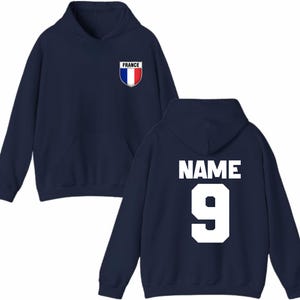 May include: Navy blue hoodie with a front pocket and hood. The front features a small patch with the French flag and the word "FRANCE". The back displays the word "NAME" above the number "9" in white.