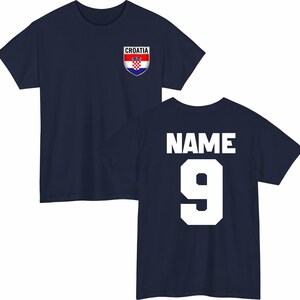 May include: Navy blue t-shirt with the Croatian flag emblem on the front and the word "NAME" and the number "9" on the back. The Croatian flag emblem is red, white, and blue. The text and number are white.
