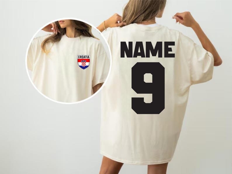 May include: Cream-colored oversized t-shirt with the word "NAME" and the number "9" in black on the back. A small Croatian flag emblem is on the front. The shirt has short sleeves and a relaxed fit.