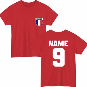 May include: Red t-shirt with a French flag emblem on the chest. The back of the shirt displays the word "NAME" above the number "9" in white block letters. A sporty design.
