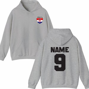 May include: A light gray hoodie with a front pocket and a hood. The front features a Croatia crest and the word "CROATIA". The back displays the word "NAME" above the number "9" in black.