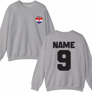May include: A heather gray sweatshirt with the word "CROATIA" above a Croatian flag emblem on the front. The back of the sweatshirt displays the word "NAME" above the number "9" in black.