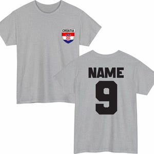 May include: A heather gray t-shirt with the Croatian flag emblem on the front and the word "CROATIA" above it. The back of the shirt displays the word "NAME" above the number "9" in black.