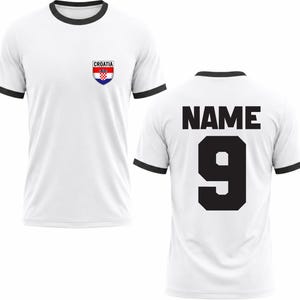 Puede incluir: Camiseta blanca con ribetes negros en el cuello y las mangas. La parte delantera presenta un emblema de la bandera croata y la palabra "CROATIA". La parte trasera muestra la palabra "NAME" sobre el n&uacute;mero "9" en negro.