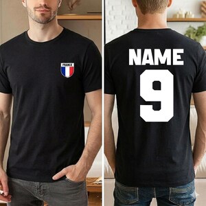 May include: Black t-shirt with a small France flag emblem on the front. The back of the shirt displays the word "NAME" above the number "9" in white block letters. The shirt is a crew neck style.