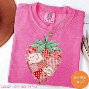 Peut inclure: Un t-shirt rose vif à manches courtes orné d'un grand motif de fraise composé de divers patchs en tissu rouge et blanc à motifs avec des bords effilochés. Le sommet feuillu vert de la fraise est en tissu vichy vert et blanc.