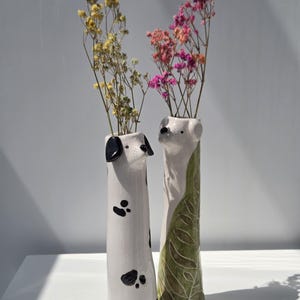 May include: A white ceramic mug with a black handle and the text "But First, Coffee" in a bold, black font. The mug is set against a blurred background, suggesting a cozy setting. The mug appears to be approximately 4 inches tall.