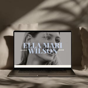May include: A laptop displaying a black and white portrait of a smiling person on its screen. The text ELLA MARI WILSON is centered in large serif font, with the words CONTENT and CREATOR positioned to the left and right of the name.