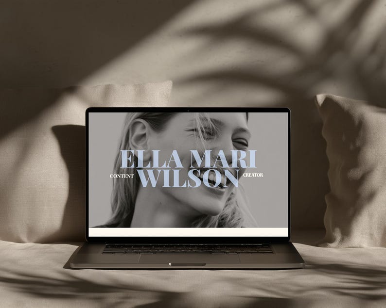 May include: A laptop displaying a black and white portrait of a smiling person on its screen. The text ELLA MARI WILSON is centered in large serif font, with the words CONTENT and CREATOR positioned to the left and right of the name.