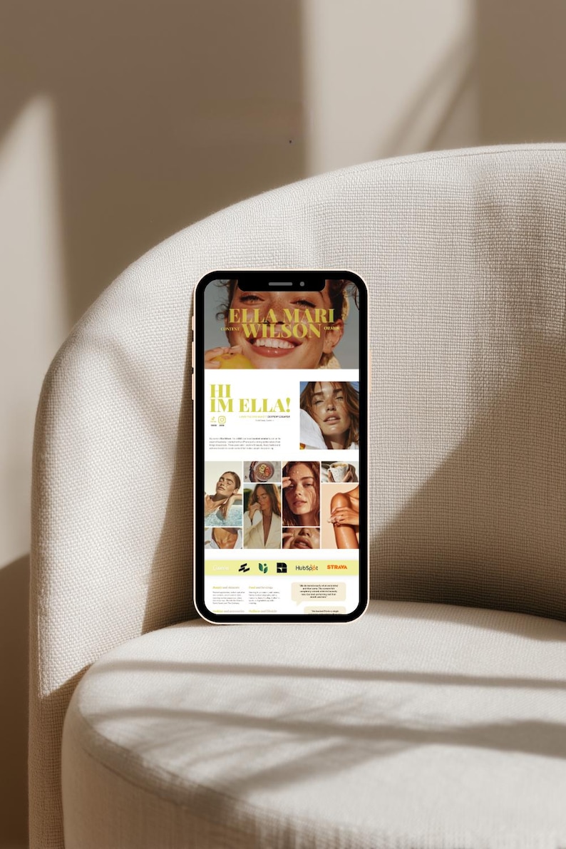 May include: A smartphone displays a website with the text "ELLA MARI WILSON" and "HI IM ELLA!" The website features multiple images of a woman, with a light yellow and white color scheme. The phone is resting on a beige armchair.