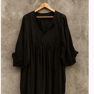 May include: A black dress with a V-neck and long sleeves hangs on a wooden hanger. The dress has a gathered waist and a flowing skirt. The fabric appears lightweight and slightly sheer, suggesting a casual or bohemian style.