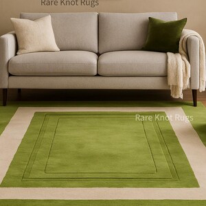 May include: A modern living room scene featuring a light gray sofa with cream and green accent pillows and a cream-colored throw. A rectangular green rug with a cream border is centered in front of the sofa. The text "Rare Knot Rugs" is visible.