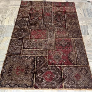 May include: A rectangular patchwork rug with a mix of brown, burgundy, and tan tones. The rug is composed of various rectangular and square patches, each with unique patterns and textures. The edges are stitched together with a contrasting thread, creating a textured border.
