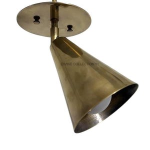 Puede incluir: Un foco de color latón con forma de cono. El foco está montado sobre una base circular con dos tornillos pequeños. El texto "DIVINE COLLECTION 01" es visible en el cono. La bombilla es visible dentro del cono.